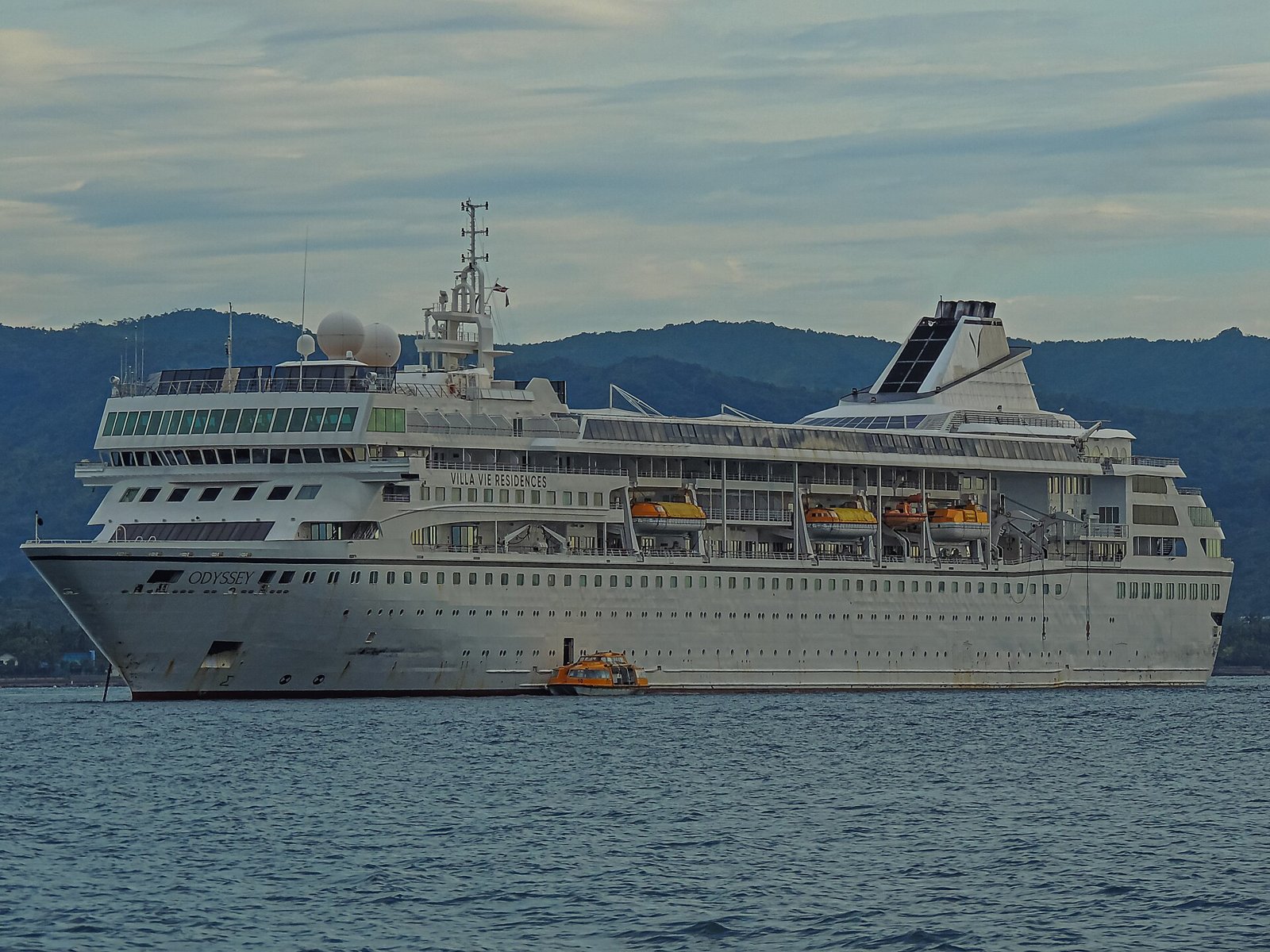 The Villa Vie Odyssey residential cruise ship at anchor with mountains behind it